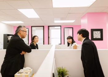 A group of Asian colleagues engaged in a lively discussion in a modern office setting.