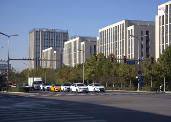 A city intersection with cars, traffic lights, and modern office buildings under a clear day sky.