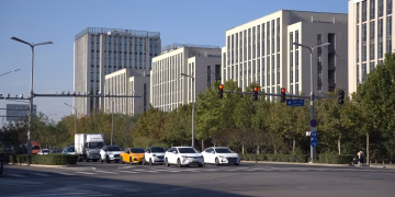 A city intersection with cars, traffic lights, and modern office buildings under a clear day sky.