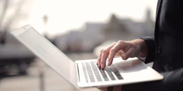 A business professional typing on a laptop in an outdoor setting, symbolizing remote work.