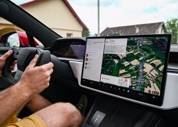 Man driving Tesla using GPS on touchscreen dashboard for navigation.