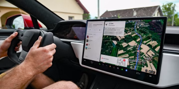 Man driving Tesla using GPS on touchscreen dashboard for navigation.
