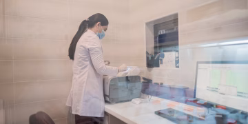 Woman in a lab coat examines equipment in a laboratory environment, Baku, Azerbaijan.
