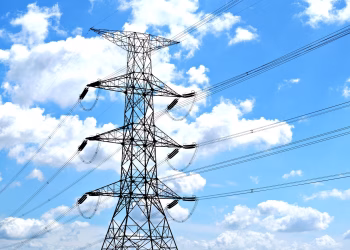 Electricity pylon with high voltage lines set against a vibrant blue sky with clouds.