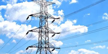 Electricity pylon with high voltage lines set against a vibrant blue sky with clouds.