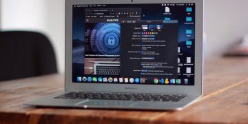 Open MacBook Air with apps and web browser on screen, placed on a wooden table indoors.