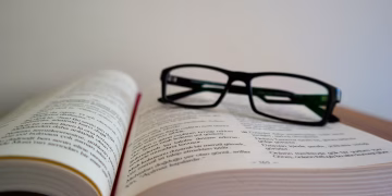 An open book with eyeglasses resting on top, symbolizing learning and education.