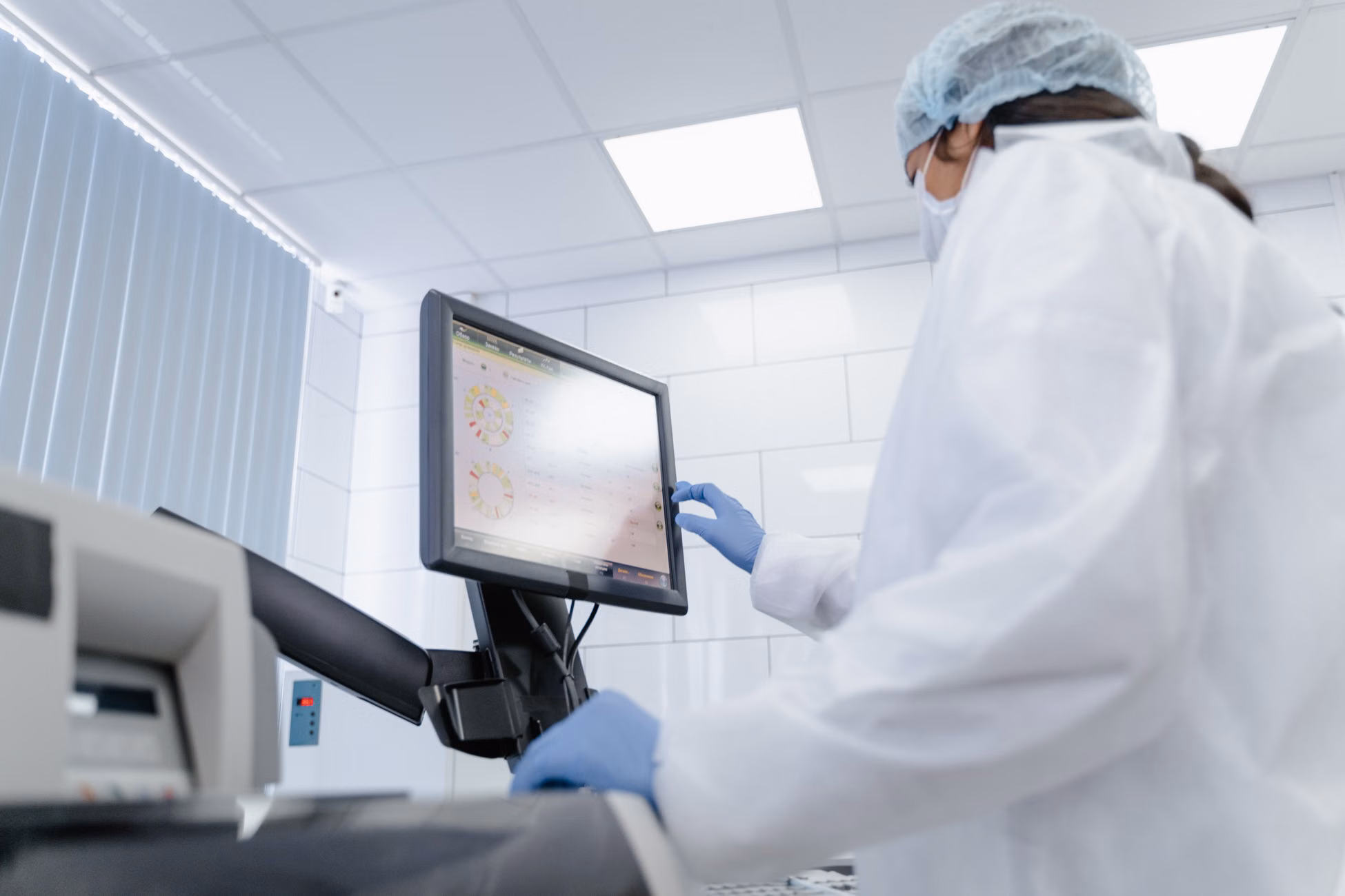 Woman in lab coat using touchscreen monitor in a modern laboratory setting.