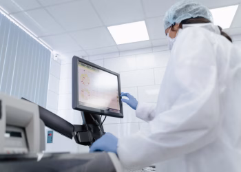 Woman in lab coat using touchscreen monitor in a modern laboratory setting.