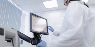 Woman in lab coat using touchscreen monitor in a modern laboratory setting.