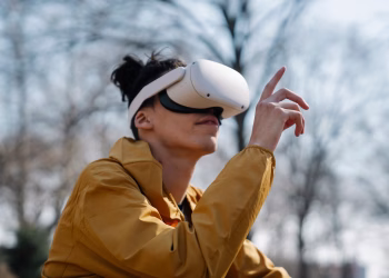 A young adult using a virtual reality headset outdoors, experiencing immersive technology in a natural setting.
