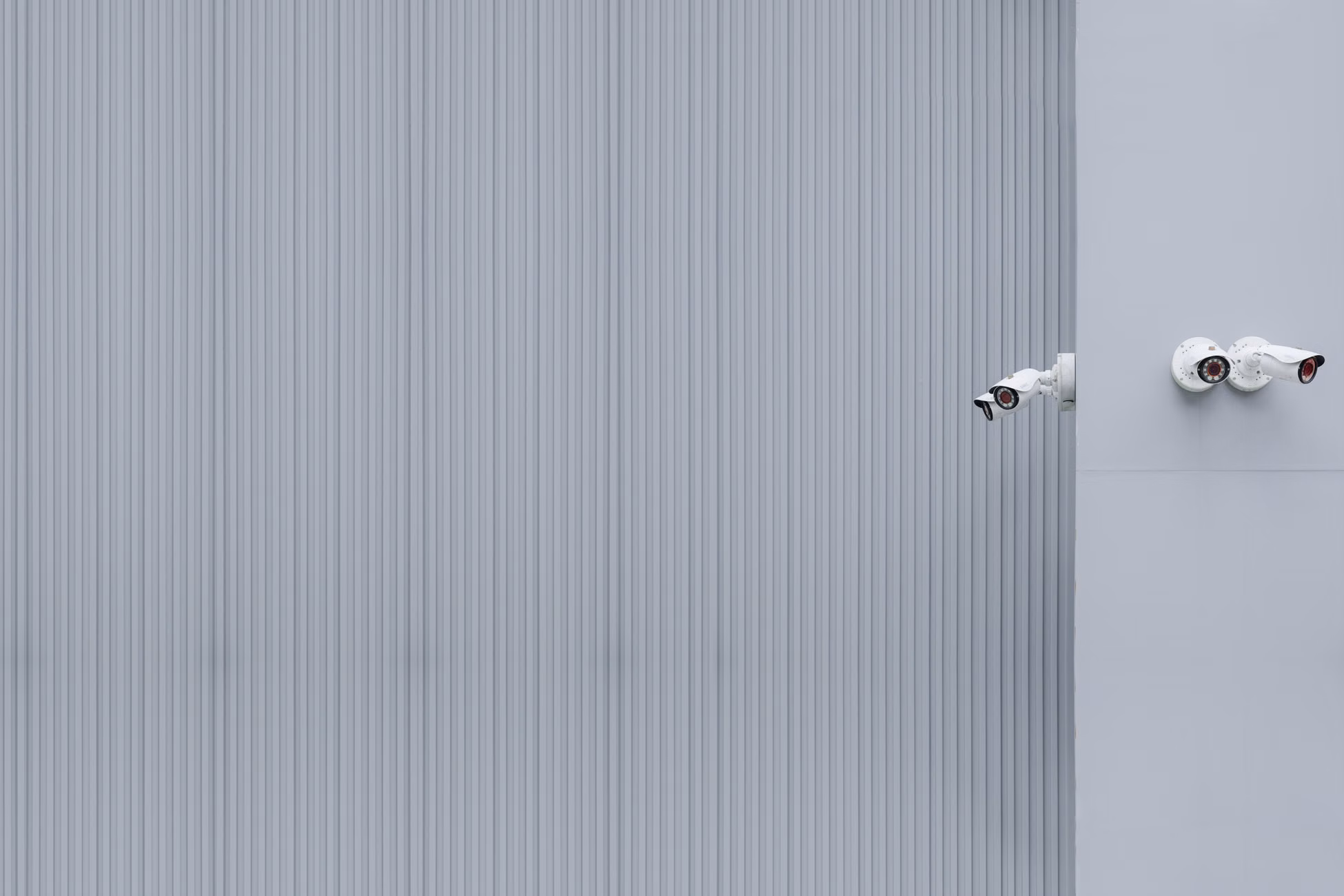 Two security cameras on a gray corrugated wall illustrating minimalism and surveillance.