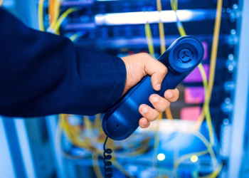 Close-up of a hand holding a telephone receiver in a server room emphasizing technology.