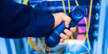 Close-up of a hand holding a telephone receiver in a server room emphasizing technology.