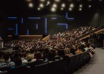 A large audience attentively listens to a speaker at a conference in Oradea, Romania.