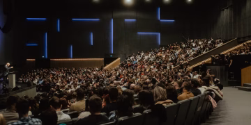 A large audience attentively listens to a speaker at a conference in Oradea, Romania.