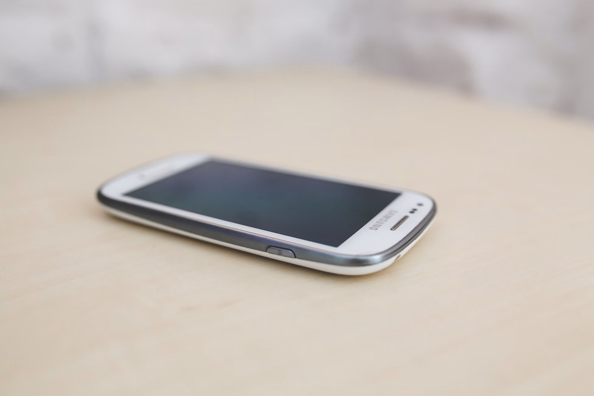 Close-up of a smartphone placed on a light wooden surface, showcasing its side view.