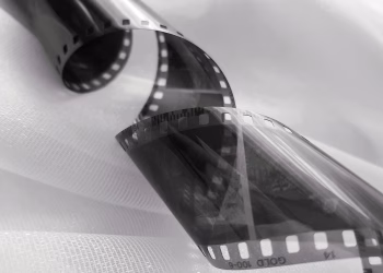 Close-up of a black and white film strip curling on white fabric, evoking nostalgia.