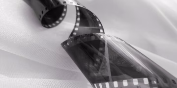 Close-up of a black and white film strip curling on white fabric, evoking nostalgia.