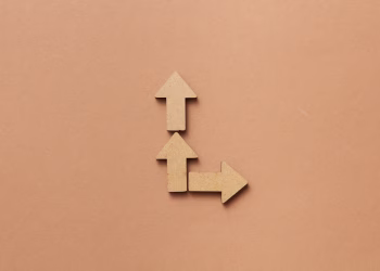 Three cardboard arrows arranged on a brown background, symbolizing direction and choice.