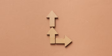 Three cardboard arrows arranged on a brown background, symbolizing direction and choice.