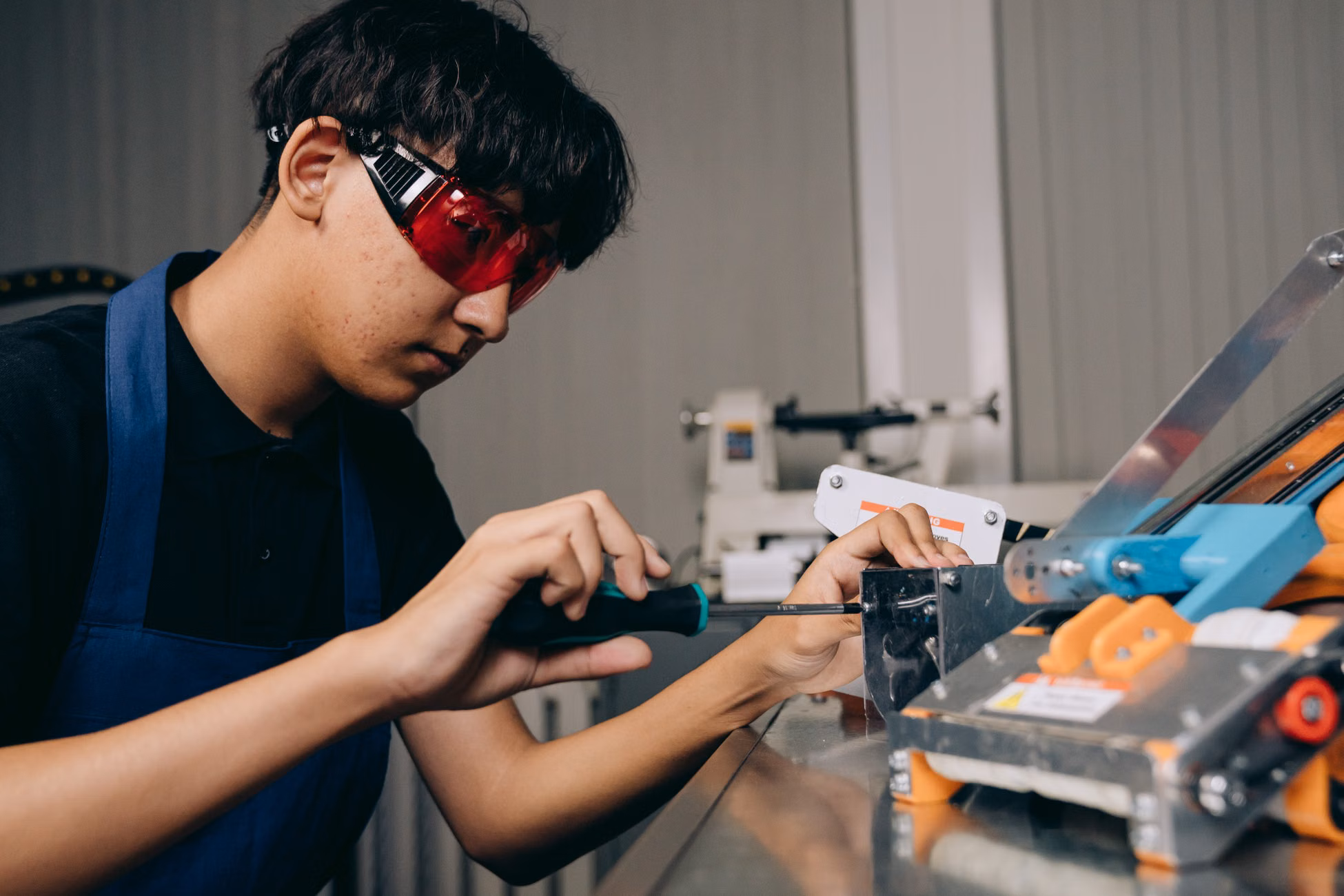 Focused young engineer working on machinery with precision tools and safety glasses indoors.
