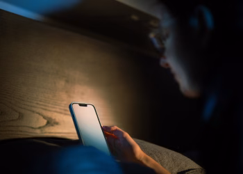 A person engages with a smartphone in a cozy, low light environment, suggesting a tech-savvy lifestyle.