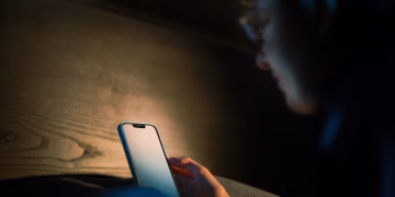 A person engages with a smartphone in a cozy, low light environment, suggesting a tech-savvy lifestyle.