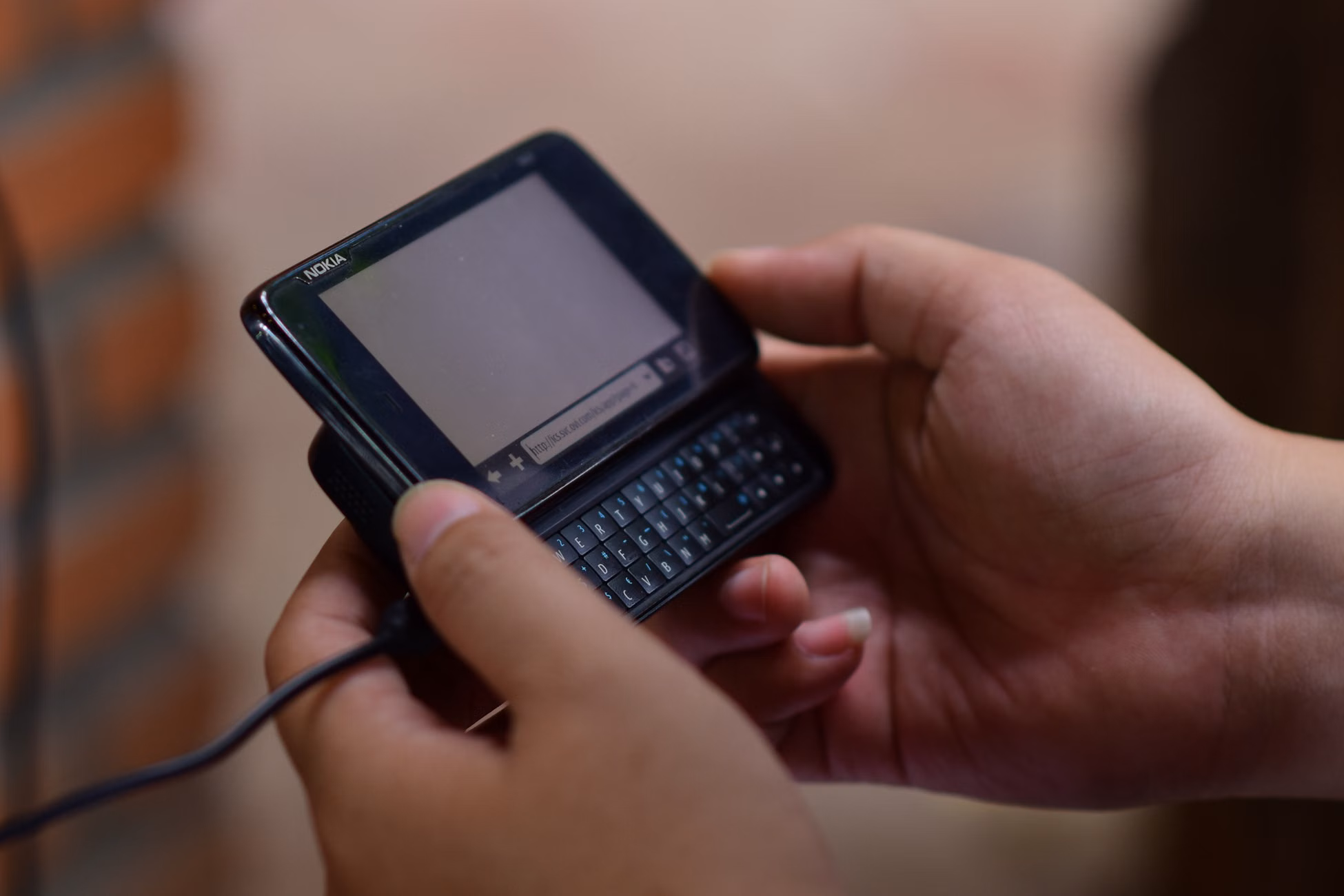Hands operating a vintage slide-out keyboard mobile phone indoors. Close-up view.