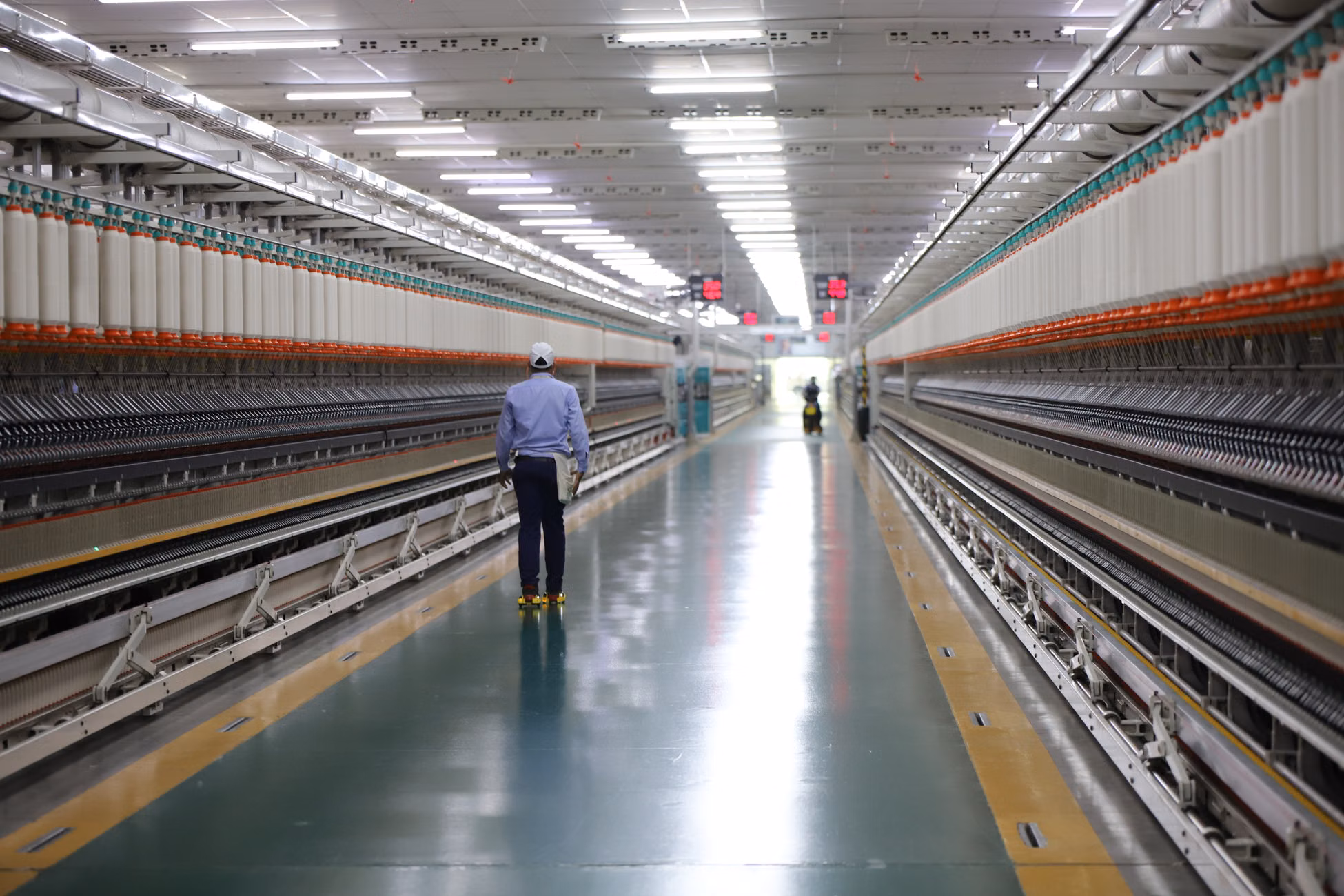 A worker walks through a wide hallway in an industrial textile plant, India.