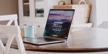 A sleek laptop on a wooden table with a mug, exemplifying a modern home workspace.