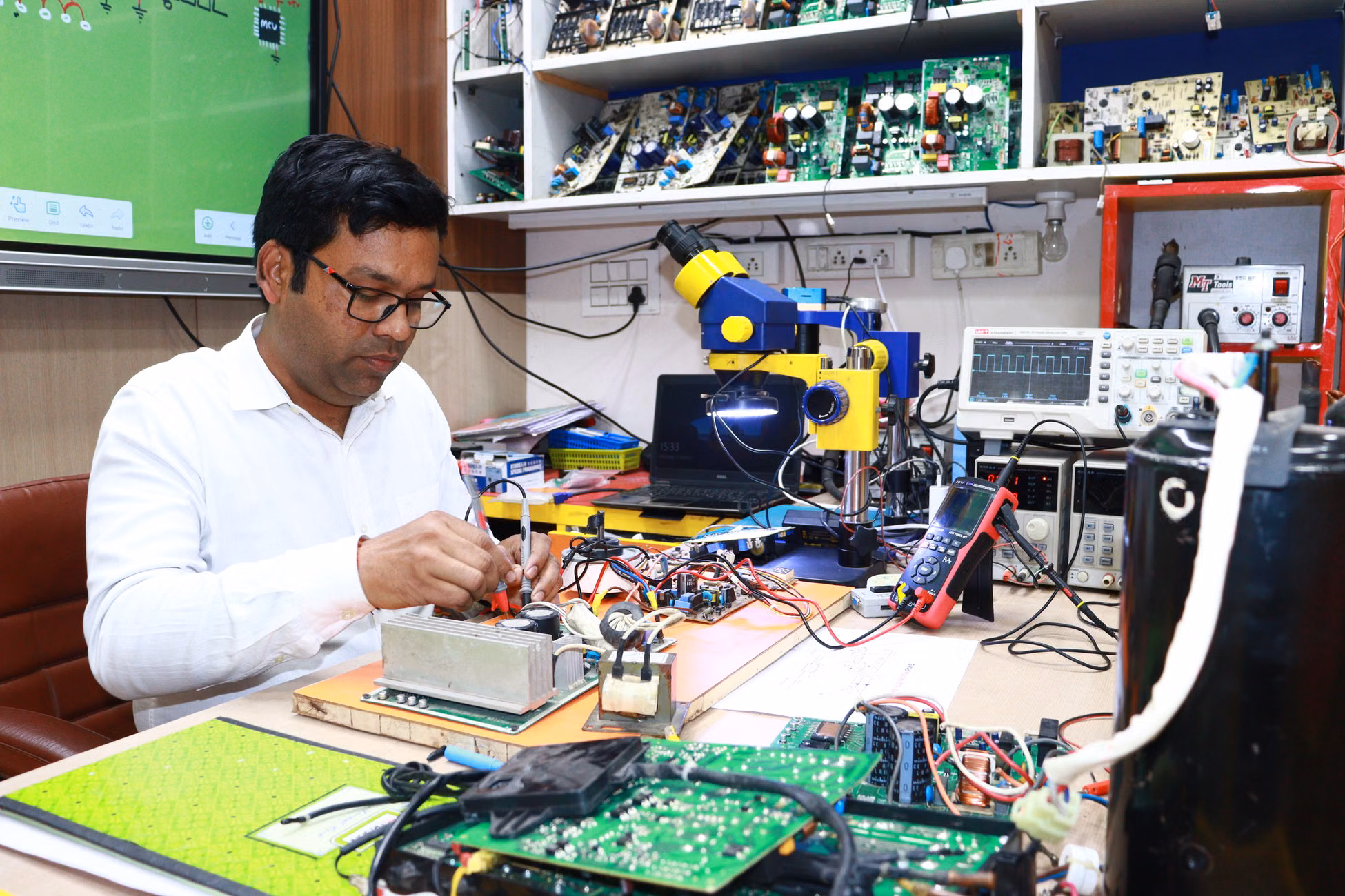 An electronics engineer working on circuit board repairs in a tech workshop filled with tools and equipment.