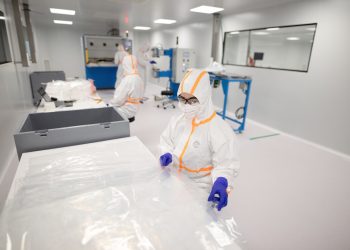 Workers in protective suits inside a cleanroom.