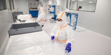 Workers in protective suits inside a cleanroom.