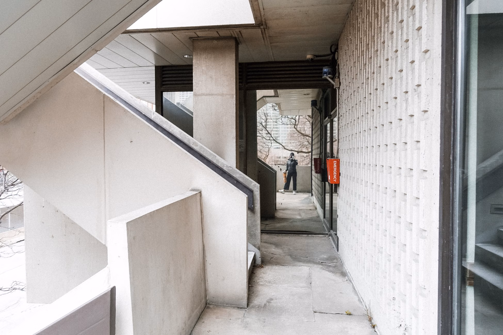 Concrete corridor with stairs in urban setting, featuring an adult person in the distance.