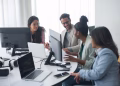 A diverse team engages in discussion around computers in a modern office setting.