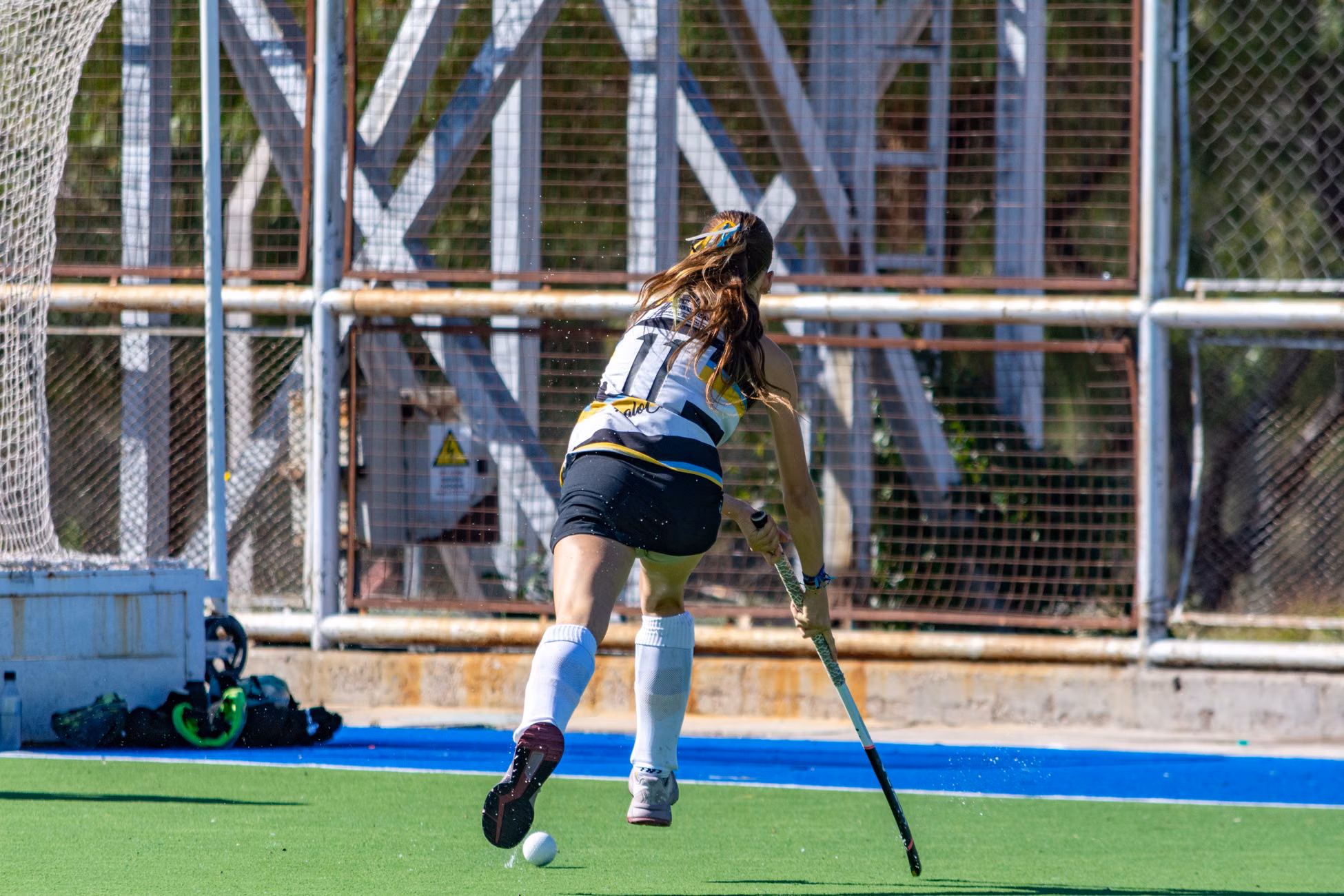 Female field hockey player running with the ball on a sunny day on the field.