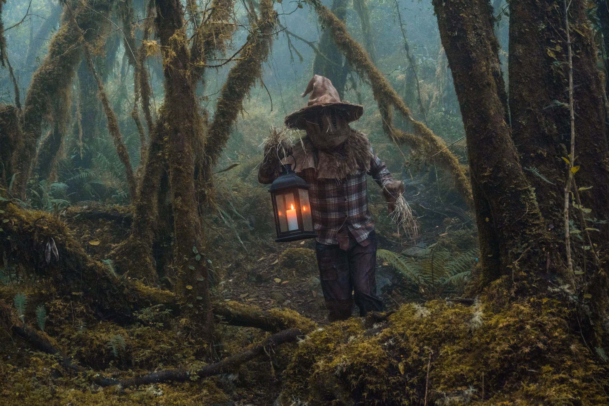 A person in a scarecrow costume holding a lantern among foggy trees in Choachí, Colombia.