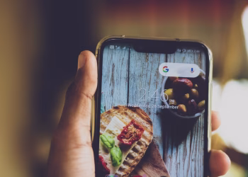 Close-up of a hand holding a smartphone displaying a food image on its screen, indoors.