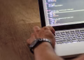 A developer's hand interacting with code on a laptop screen in a workspace setting.