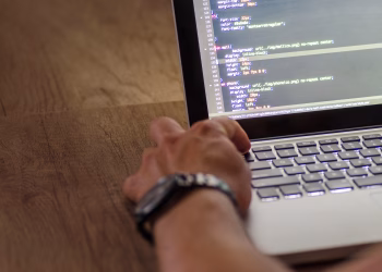 A developer's hand interacting with code on a laptop screen in a workspace setting.