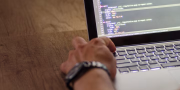 A developer's hand interacting with code on a laptop screen in a workspace setting.