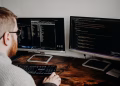 Software developer working on code with dual monitors in a home office setting.