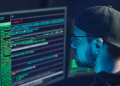 A cybersecurity expert inspecting lines of code on multiple monitors in a dimly lit office.