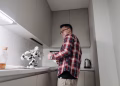 Asian man smiling while playing with a robot in a modern kitchen setting.