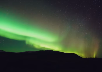 From below picturesque view of colorful shiny polar lights illuminating sky over mount silhouette at dusk
