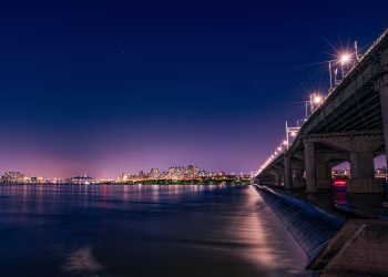 Vibrant night view of Seoul with illuminated bridge and city skyline reflecting on Han River.