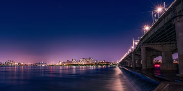 Vibrant night view of Seoul with illuminated bridge and city skyline reflecting on Han River.