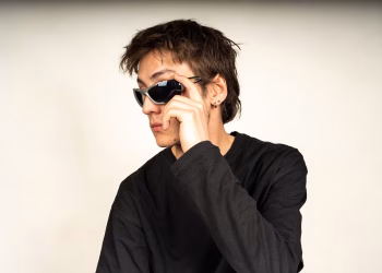 Modern portrait of a young adult wearing black sunglasses and a dark shirt, exuding style and confidence.