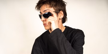 Modern portrait of a young adult wearing black sunglasses and a dark shirt, exuding style and confidence.